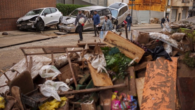 People walk past cars piled up in an area affected by flooding in Chiva, Spain, Friday, Nov. 1, 2024. (AP Photo/Manu Fernandez)