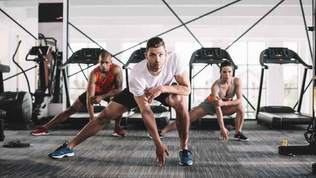 handsome trainer looking at camera while doing lunges exercise together with multicultural athletes