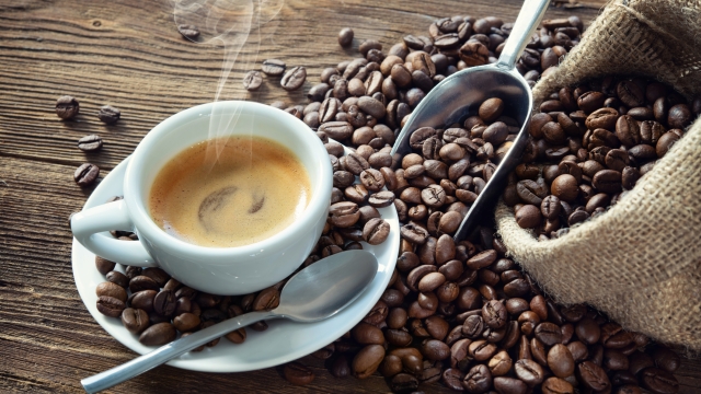 Cup of espresso with coffee beans, bag, scoop and steam on rustic wooden background