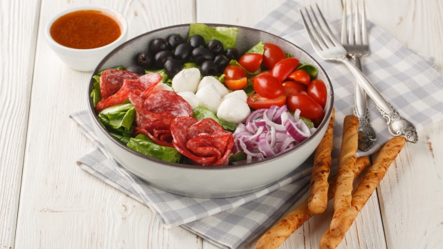 Pizza bowl salad with salami sausages, mozzarella cheese, tomatoes, olives, onions, romaine lettuce and spicy dressing served with breadsticks close-up on a table. Horizontal