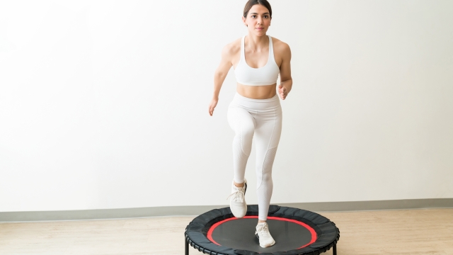 Dedicated young woman in white sportswear trampolining against wall during high intensity interval training