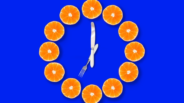 Clocks made of half cut tangerines with arrows made of fork and knife that shows 7 o'clock on a bright blue background. Concept of good healthy morning.