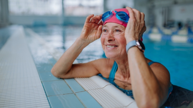 A happy senior woman in swimming pool, leaning on edge.