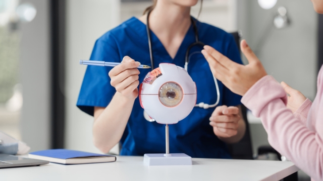 Female Caucasian ophthalmologist explains about eye diseases using the eye model with an Asian female patient At the table in the hospital examination room, Glaucoma, Cataract, Diabetic Retinopathy