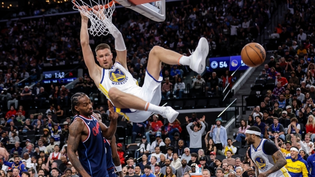 Golden State Warriors' Krystaps Porzingis (7) hangs from the rim after following a missed Stephen Curry (30) shot attemps with a dunk in the first half of an NBA play-in tournament game in Inglewood, Calif., on Wednesday, April 15, 2026. (Carlos Avila Gonzalez/San Francisco Chronicle via AP)