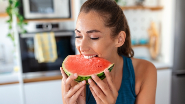 Young woman eats a slice of watermelon in the kitchen. Portrait of young woman enjoying a watermelon.