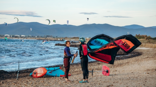  Two wing foilers preparing equipment on Plage de l Almanarre beach with kitesurfers and Mediterranean coast in background