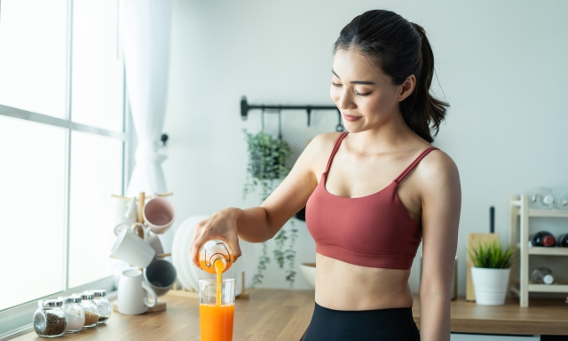 Portrait of Asian beautiful woman hold and pour orange juice in glass. Attractive sport girl in sportswear holding a cup of water, enjoy drink and eat healthy foods for health after exercise in house.