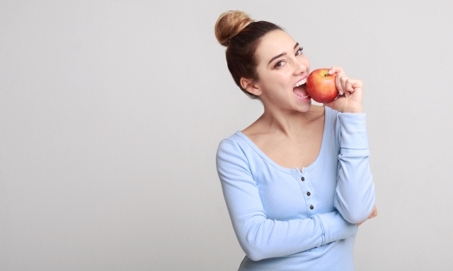 Healthy eating. Pretty girl biting fresh apple over grey background, copy space