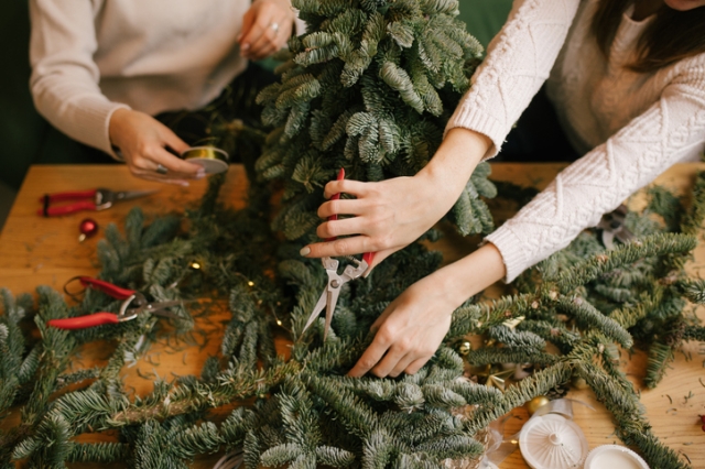 Two young women making Christmas tree using natural pine branches on a workshop.