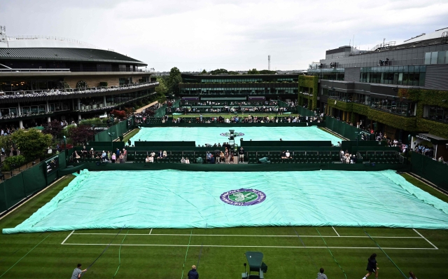 Members of the ground staff pull the cover on court as they rain starts to fall on the first day of the 2023 Wimbledon Championships at The All England Tennis Club in Wimbledon, southwest London, on July 3, 2023. (Photo by SEBASTIEN BOZON / AFP) / RESTRICTED TO EDITORIAL USE
