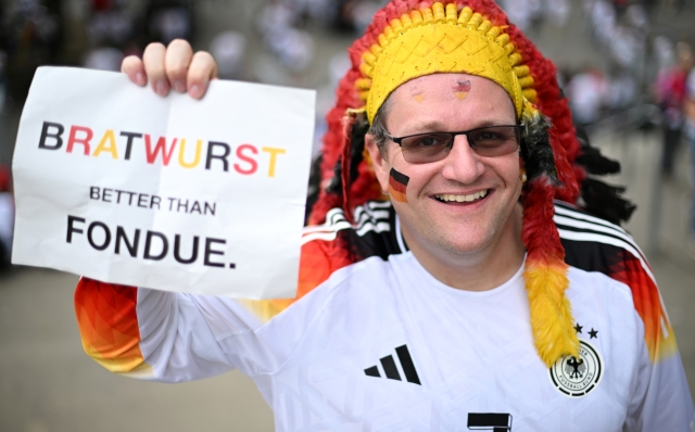 FRANKFURT AM MAIN, GERMANY - JUNE 23: A fan of Germany poses for a photo with s sign which reads "Bratwurst, Better Than Fondue" prior to the UEFA EURO 2024 group stage match between Switzerland and Germany at Frankfurt Arena on June 23, 2024 in Frankfurt am Main, Germany. (Photo by Justin Setterfield/Getty Images)