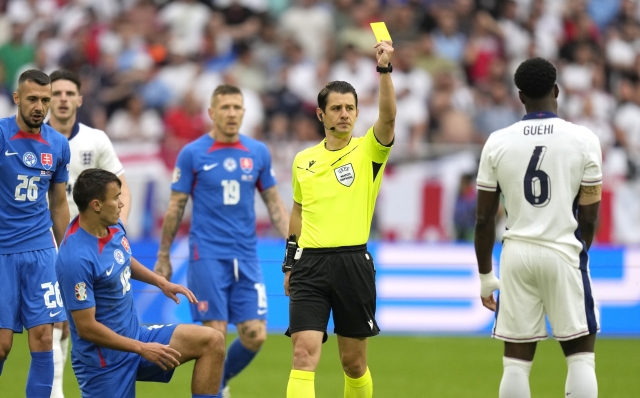 Referee Halil Umut Meler shows a yellow card to England's Marc Guehi, right, during a round of sixteen match between England and Slovakia at the Euro 2024 soccer tournament in Gelsenkirchen, Germany, Sunday, June 30, 2024. (AP Photo/Ariel Schalit)