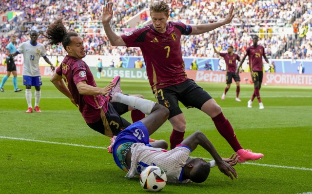 France's Marcus Thuram, bottom, falls as he vies for the ball with Belgium's Kevin De Bruyne, right, and Arthur Theate during a round of sixteen match between France and Belgium at the Euro 2024 soccer tournament in Dusseldorf, Germany, Monday, July 1, 2024. (AP Photo/Hassan Ammar)