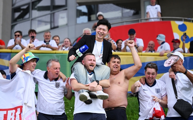 DUSSELDORF, GERMANY - JULY 06: Fans of England react as they interact with journalist Kan Chen of iQiyi Sports China on the outside of the stadium prior to the UEFA EURO 2024 quarter-final match between England and Switzerland at Düsseldorf Arena on July 06, 2024 in Dusseldorf, Germany. (Photo by Clive Mason/Getty Images)
