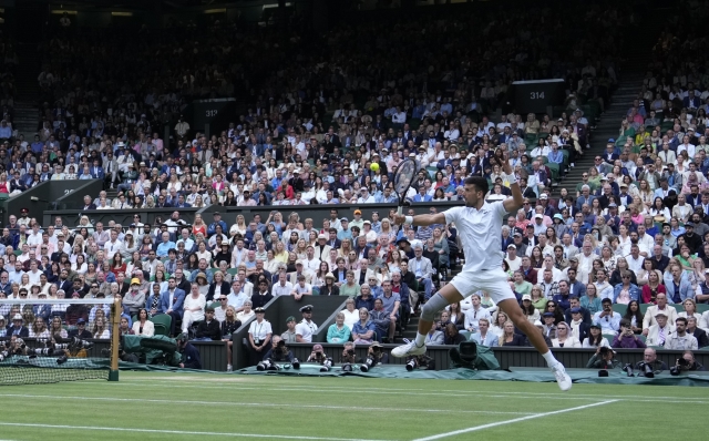 Novak Djokovic of Serbia leaps as he plays a backhand Lorenzo Musetti of Italy during their semifinal match at the Wimbledon tennis championships in London, Friday, July 12, 2024. (AP Photo/Mosa'ab Elshamy)