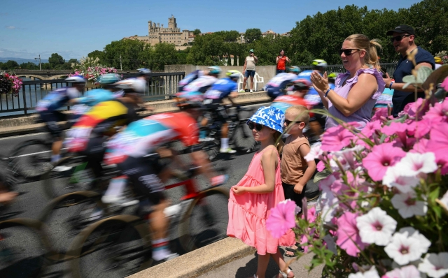 The pack of riders (peloton) cycles across the Georges Fontes bridge into Beziers during the 16th stage of the 111th edition of the Tour de France cycling race, 188,6 km between Gruissan and Nimes, southern France, on July 16, 2024. (Photo by Marco BERTORELLO / AFP)