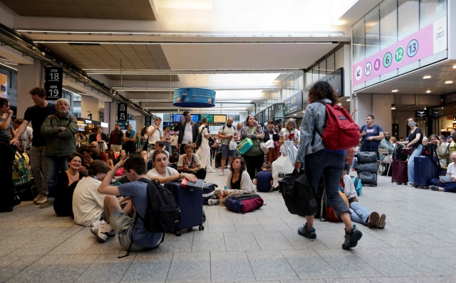 Passengers wait for their train departures at the Gare Montparnasse train station in Paris on July 26, 2024 as France's high-speed rail network was hit by malicious acts disrupting the transport system hours before the opening ceremony of the Paris 2024 Olympic Games. According to SNCF a massive attack on a large scale hit the TGV network and many routes will have to be cancelled. SNCF urged passengers to postpone their trips and stay away from train stations. (Photo by Thibaud MORITZ / AFP)