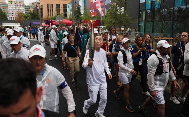 Former Secretary-General of the UN Ban Ki-moon (C) runs with the Olympic torch during the Olympic village torch relay in the Olympic Village in Paris on July 26, 2024, ahead of the Paris 2024 Olympic Games. (Photo by Leah Millis / POOL / AFP)