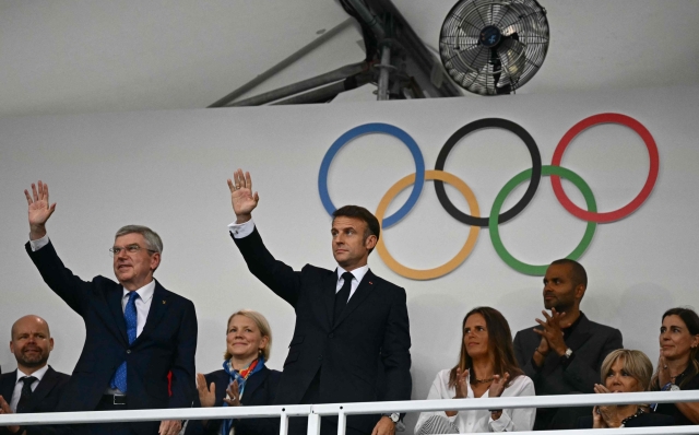 France's President Emmanuel Macron (R) and the President of the International Olympic Committee (IOC) Thomas Bach wave as they arrive to attend the opening ceremony of the Paris 2024 Olympic Games in Paris on July 26, 2024. (Photo by Loic VENANCE / POOL / AFP)