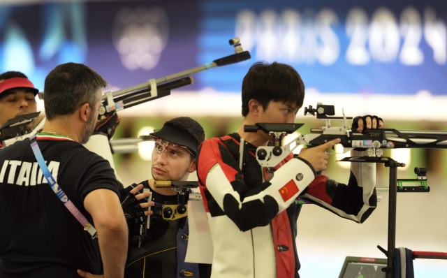 Italy's Dennis Danilo Sollazzo talks to his coach during the 10m Air Rifle Men pre event training at the 2024 Summer Olympics, Saturday, July 27, 2024, in Chateauroux, France. (AP Photo/Manish Swarup)
