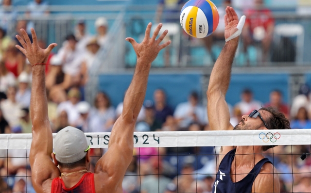 Italy's #01 Alex Ranghieri spikes the ball as Chile's #01 Marco Grimalt blocks in the men's pool B beach volleyball match between Italy and Chile during the Paris 2024 Olympic Games at the Eiffel Tower Stadium in Paris on August 2, 2024. (Photo by Thomas SAMSON / AFP)