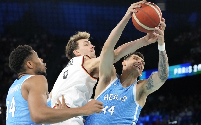 Isaac Bonga, center, of Germany, and Dinos Mitoglou, right, of Greece, reach for a rebound as Giannis Antetokounmpo, of Greece, watches during a men's basketball game at the 2024 Summer Olympics, Tuesday, Aug. 6, 2024, in Villeneuve-d'Ascq, France. (AP Photo/Michael Conroy)