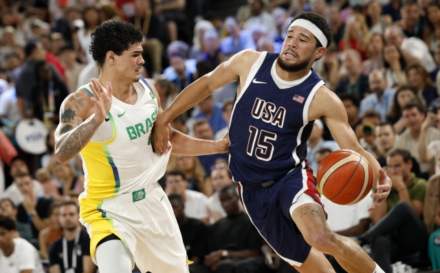 epa11531666 Devin Booker of the US (R) and Gui Santos of Brazil in action during the men's quarterfinal match between Brazil and USA in the Basketball competitions in the Paris 2024 Olympic Games, at the South Paris Arena in Paris, France, 06 August 2024.  EPA/CAROLINE BREHMAN