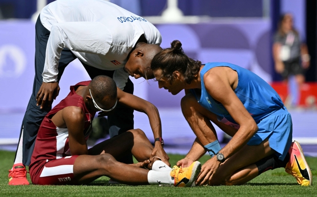 Italy's Gianmarco Tamberi (R) checks on Qatar's Mutaz Essa Barshim (L) holding his calf following an injury while competing in the men's high jump qualification of the athletics event at the Paris 2024 Olympic Games at Stade de France in Saint-Denis, north of Paris, on August 7, 2024. (Photo by Andrej ISAKOVIC / AFP)