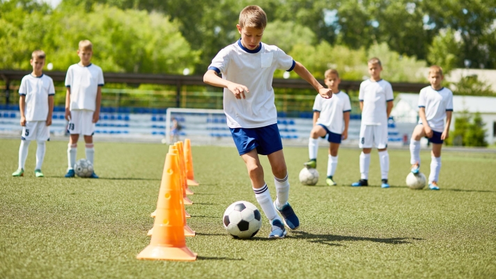 Portrait of boy in junior football team  leading ball between cones during  practice in field on sunny day