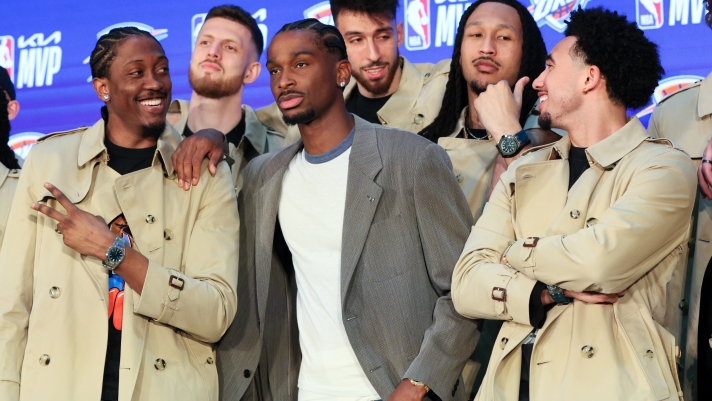 Oklahoma City Thunder guard Shai Gilgeous-Alexander, center, poses with teammates Jalen Williams, left, Isaiah Hartenstein, second from left, Chet Holmgren, center back, Jaylin Williams, second from right, and Jared McCain, right, in Burberry trench coats bought by Gilgeous-Alexander during a news conference after he was named the NBA basketball MVP, Sunday, May 17, 2026, in Oklahoma City. (AP Photo/Nate Billings)