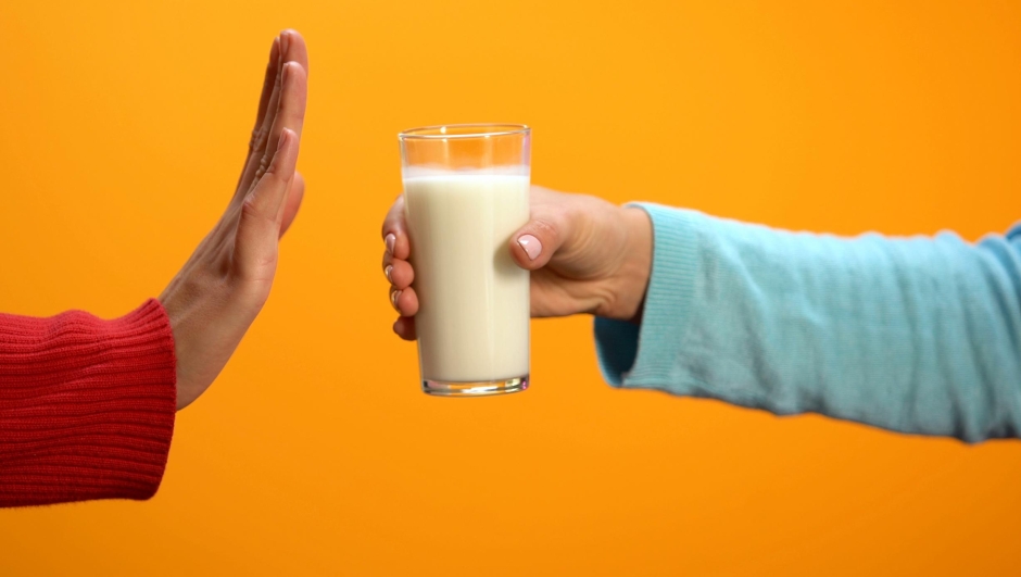 Female refusing to drink milk showing stop gesture on bright background, health