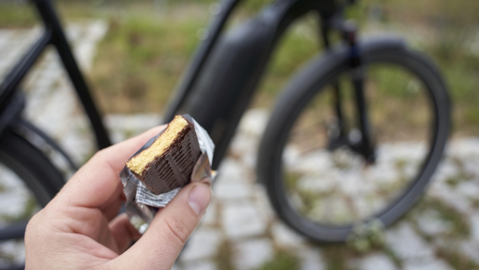 Power bar provides energy while cycling. Hand holds bitten protein food with many nutrients. Good for the muscles.