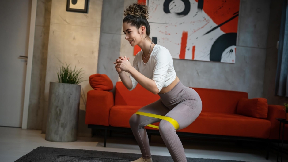 One woman beautiful female training at home in room using rubber resistance bands for legs squat and butt glutes sportswoman doing exercises alone health and fitness concept copy space full length