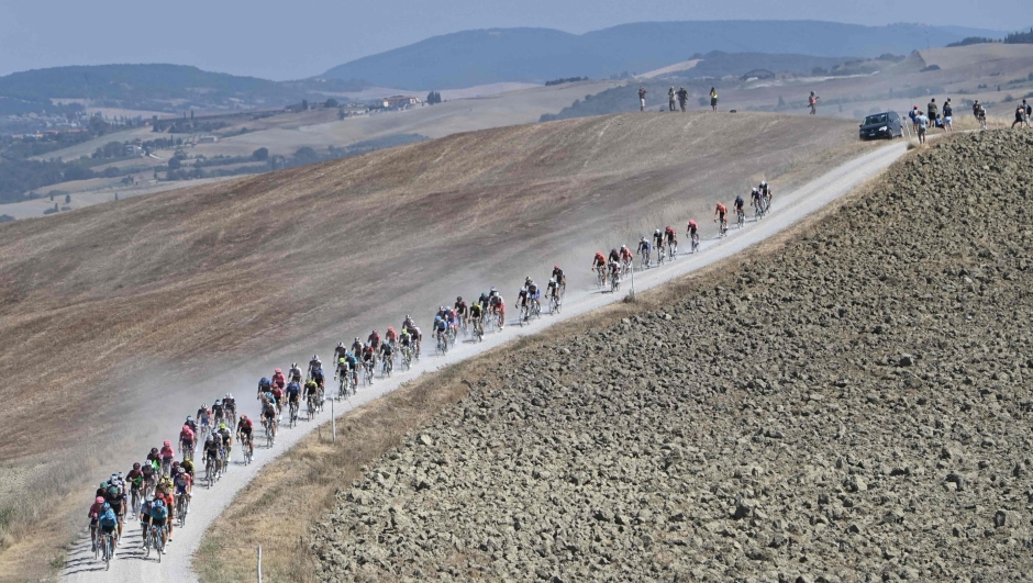 (FILES) In this file photo taken on August 1, 2020 The pack of riders pedal through a dusty gravel road during the one-day classic cycling race Strade Bianche (White Roads) around Siena, Tuscany. - If it doesn't have the history of the venerable northern European classics, the Strade Bianche, whose 17th edition takes place on Saturday in Tuscany, has found its place with its "muri", its dirt roads and the finish in the heart of Siena. (Photo by Marco BERTORELLO / AFP)