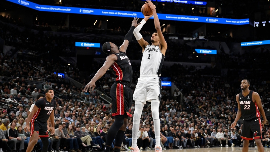 San Antonio Spurs center Victor Wembanyama (1) goes up to shoot against Miami Heat forward Bam Adebayo, center left, during the second half of an NBA basketball game, Thursday, Oct. 30, 2025, in San Antonio. (AP Photo/Darren Abate)