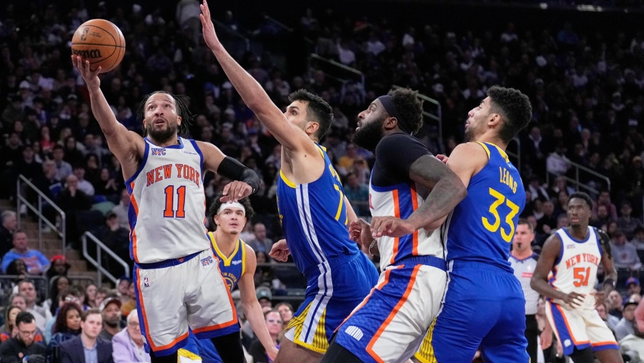 New York Knicks' Jalen Brunson (11), left, drives to the basket past Golden State Warriors defenders during the second half of an NBA basketball game Sunday, March 15, 2026, in New York. (AP Photo/Seth Wenig)