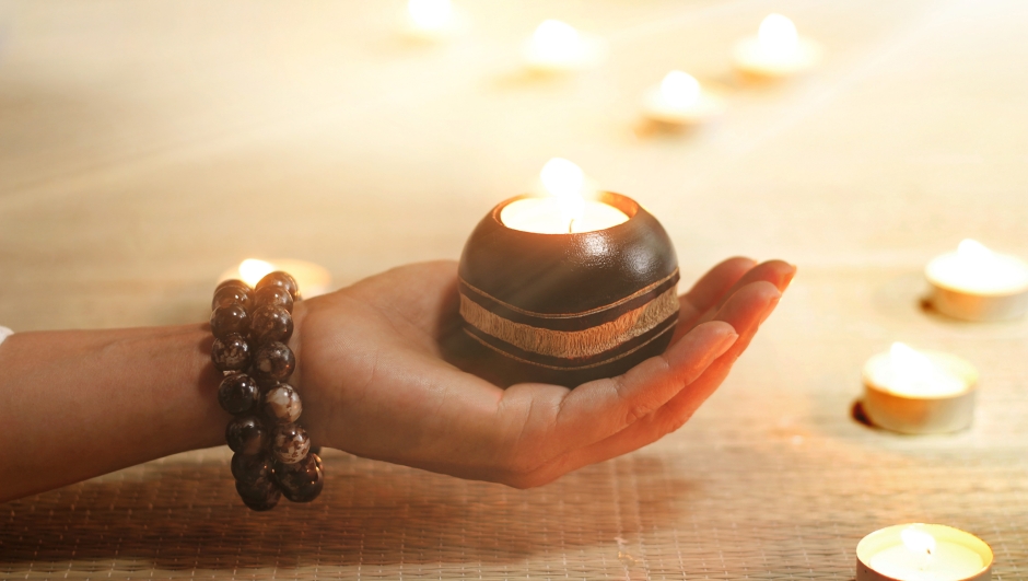 Woman hand yoga and meditation holding oil lamps in temple on candle warm glowing background