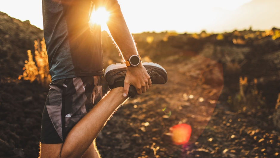 Male runner stretching leg and feet and preparing for running outdoors. Smartwatches or fitness tracker on hand. Beautiful sun light on background. Active and healthy lifestyle concept.