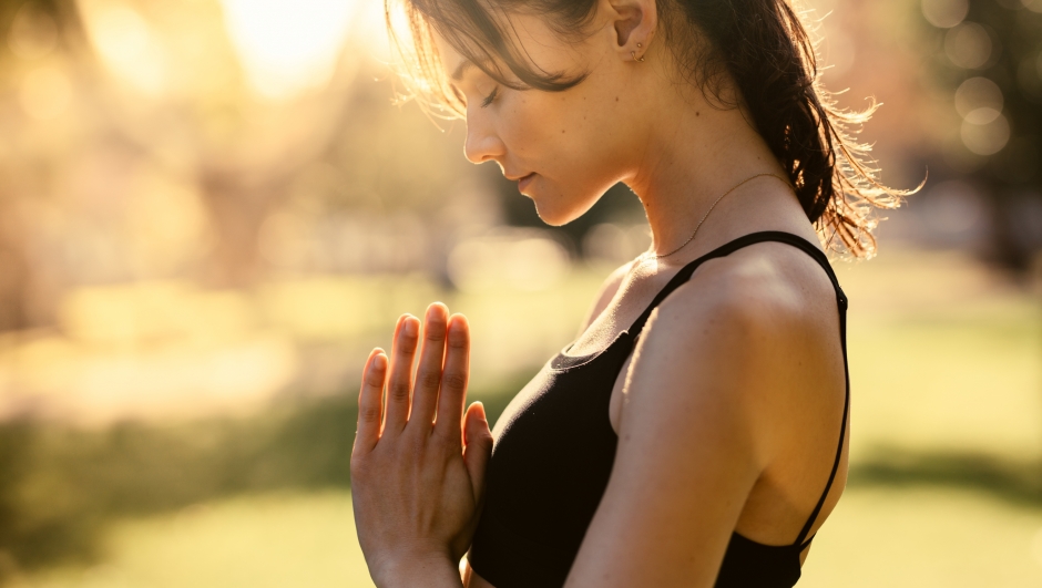 Fitness woman doing yoga with her hands joined and eyes closed. Female standing outdoors and practising meditation.