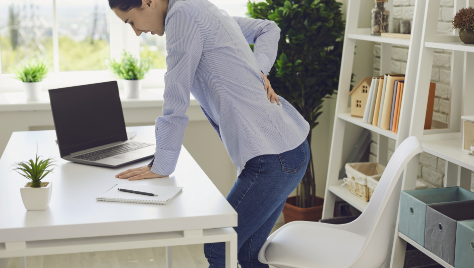 Young woman suffering from back pain at workplace, copy space text. Overworked company employee feeling backache at her desk in office