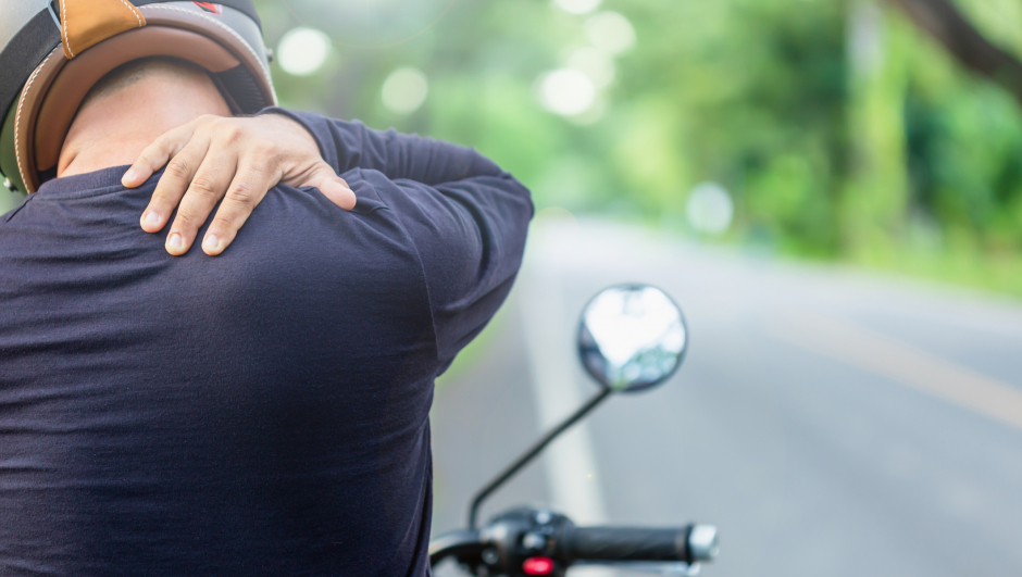 Motorcyclist with pain or tired concept : Man rider touching on his neck or shoulder and feeling tired after long ride motorcycle. Outdoor shooting on the road with copy space