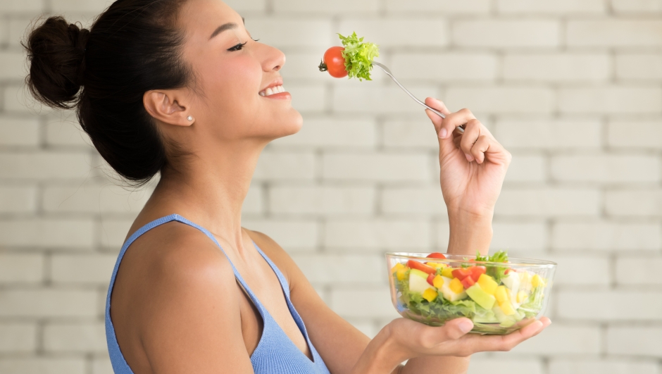 Asian woman in joyful postures with hand holding salad bowl