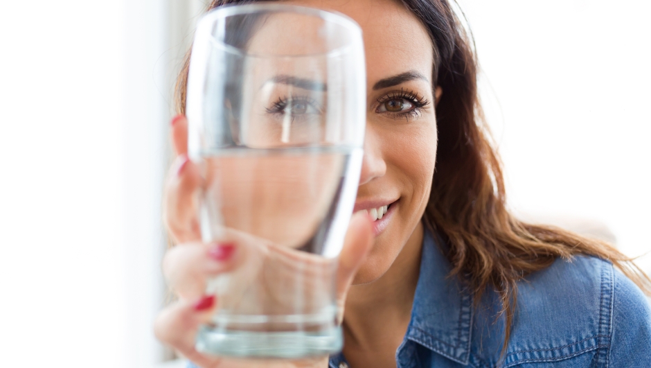 Portrait of pretty young woman smiling while looking at the camera through the glass of water at home.