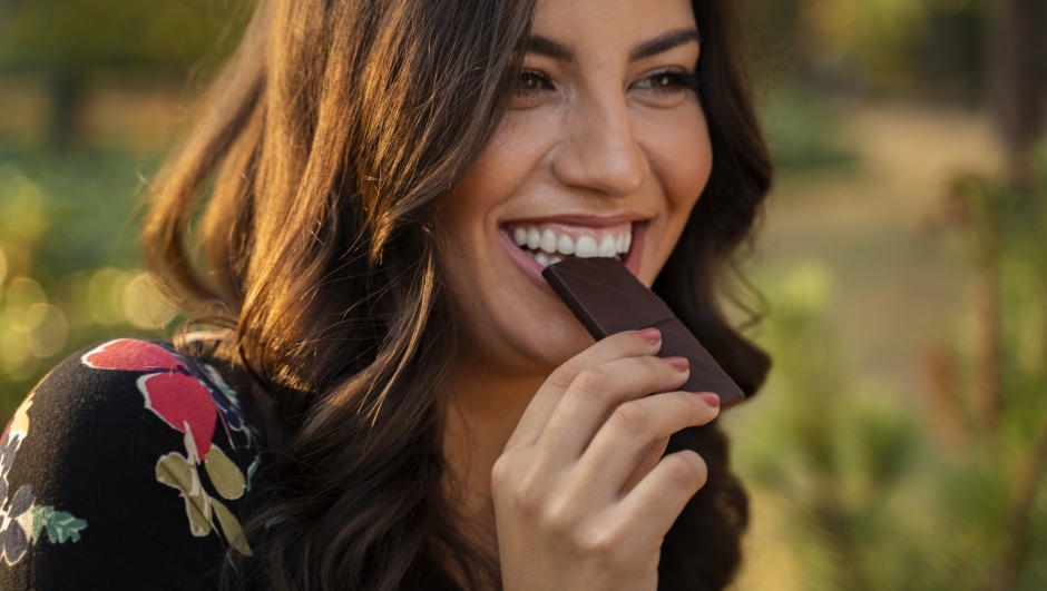 Closeup portrait of charismatic cheerful young woman eating chocolate and smiling