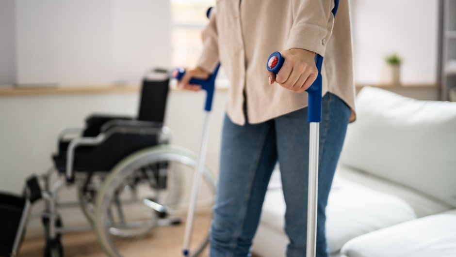 Hurt Leg Using Crutches Near Wheelchair At Home