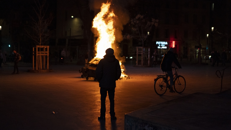 A man looks at a fire set by protesters in Marseille, southern France, Monday, March 20, 2023. The French government has survived two no-confidence votes in the lower chamber of parliament, proposed by lawmakers who objected to its push to raise the retirement age from 62 to 64. (AP Photo/Daniel Cole)