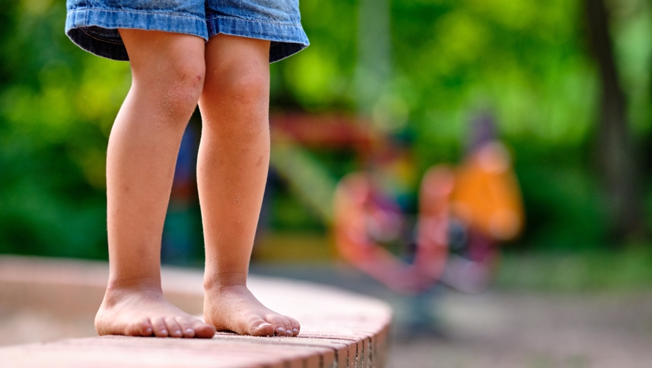 Low section of a caucasian child girl in jeans shorts who is standing barefoot on a little stone wall with sandy feet in summer