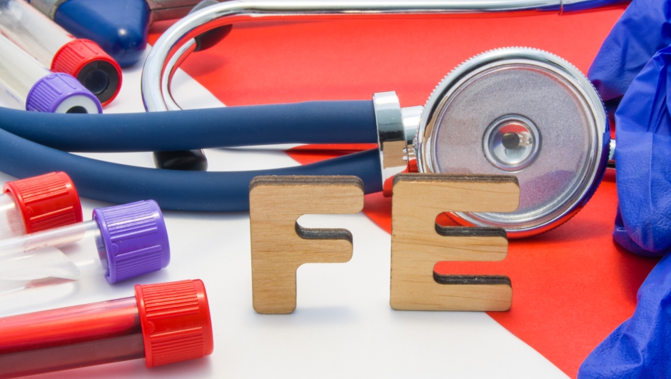 FE medical abbreviation meaning total iron or ferrum in blood in laboratory diagnostics on red background. Chemical name of FE is surrounded by medical laboratory test tubes with blood, stethoscope