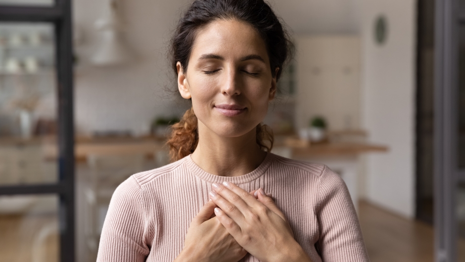 Close up of calm young Caucasian woman hold hands on heart chest feel grateful and thankful. Happy millennial female show gratitude, love and care, pray or visualize. Religion, faith concept.